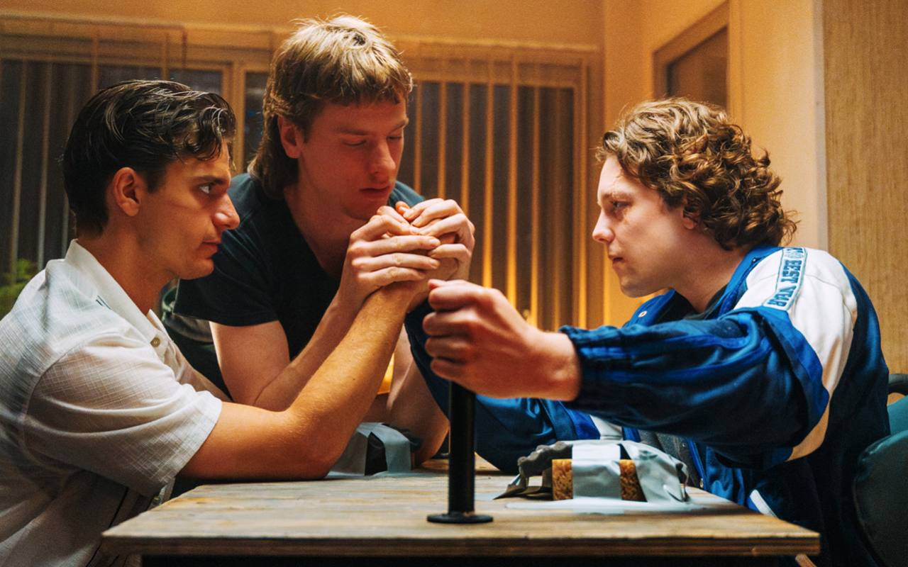 Joe Speedboot: three young men around an arm-wrestling table in warm interior light